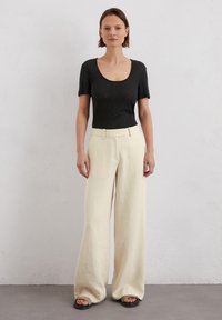 Top corto nero a maniche corte con scollatura a girocollo, abbinato a pantaloni a gamba larga di un bianco sporco. L'outfit è completato da sandali neri flat.
