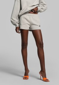 Lichtgrijze katoenen shorts met een elastische tailleband en zijzakken, gecombineerd met feloranje haksandalen. Soepele, casual uitstraling.