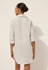 Chemise en lin gris clair, avec un col classique, des manches retroussées et un ourlet arrondi. Texture douce avec un motif de tissage visible.