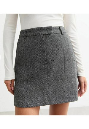 Kvinde iført en højtaljet nederdel med sort-hvidt sildebensmønster og en langærmet, hvid ribbet top.