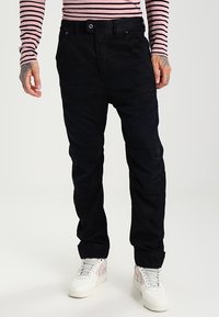 Pantalones negros ajustados con tejido texturizado, cinco bolsillos y trabillas para el cinturón. Combinados con zapatillas blancas con detalles en rosa.