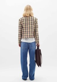 Beige kockás cropped dzseki narancssárga és fekete részletekkel, laza kék farmernadrággal párosítva. A modellen egy barna tote táska van.