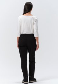 Witte driekwart mouwtop en zwarte elastische taillebroek, met een gladde textuur en een ontspannen pasvorm, gecombineerd met zwarte schoeisel.