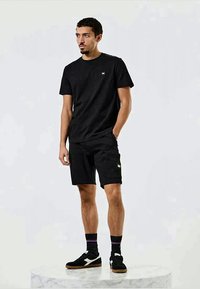Sort bomulds t-shirt med en lille logo, parret med sorte cargo shorts med lomme detaljer. Båret med sorte sneakers og stribede sokker.