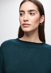 Maglione a dolcevita color verde scuro, realizzato in tessuto a maglia texturizzato. Presenta un collo a barca e delicate finiture a costine sui polsini.