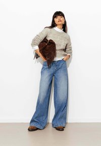 Pull en maille gris clair surdimensionné, jeans bleu à jambe large, sac à franges en suede marron et chaussures à imprimé animal. Sur fond blanc.