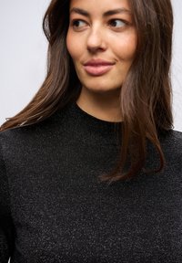 Mustat neulotut yläosat, joissa on korkea kaula-aukko ja tekstuurinen kiiltovaikutus. Materiaali näyttää sileältä, ja siinä on hienovaraisia korostuksia.