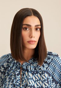 Blusa con motivo floreale blu e bianco, tessuto strutturato e scollatura con fiocco. Presenta una vestibilità ampia e dettagli plissettati sulle maniche.
