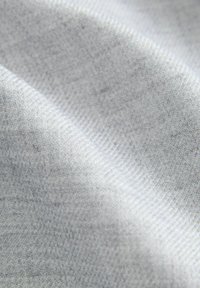 Tessuto grigio chiaro con una consistenza morbida e liscia, caratterizzato da un sottile motivo a spina di pesce. La tessitura è compatta e uniforme.