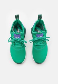 Gröna sportiga sneakers med en slät tygöverdel, kontrasterande lila detaljer, platta snören och en strukturerad vit sula.