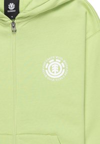 Lichtgroene ritshoodie met een zachte textuur. Heeft een ronde witte logo op de linkerborst. Standaardpasvorm, geen aanvullende accenten.