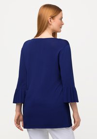 Navyblauwe tuniek met driekwart geplooide mouwen. Zachte stof, ontspannen pasvorm en een ronde halslijn. Ontworpen voor comfort en veelzijdigheid.