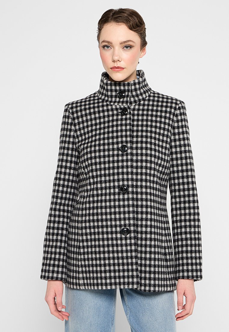 Zwart-wit houndstooth-jas met een hoge kraag en zes zwarte knopen. Gestructureerde vorm, lange mouwen en textiel met een textuur.
