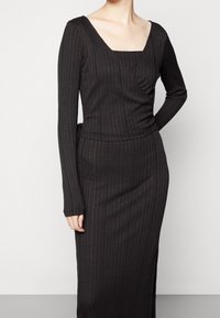 Robe noire à manches longues, en maille côtelée, avec un décolleté carré, offrant un design croisé et une silhouette ajustée, fabriquée dans un matériau doux et extensible.