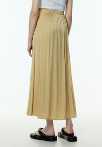 Maxi rok in lichtbeige, gemaakt van zachte stof, met een elastische tailleband en een vloeiende, geplooide ontwerp. Draag het met zwarte sandalen.