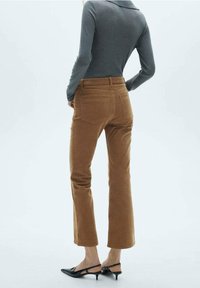 Pantalon patte d'éléphant en velours côtelé marron avec deux poches arrière, associé à un haut gris ajusté. Les chaussures sont noires avec des talons étroits.