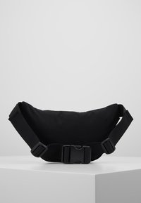 Svart nylonaxelväska med en rundad form, justerbar rem och plastspänne. Slät yta, minimalistisk design, lämplig för avslappnad användning.