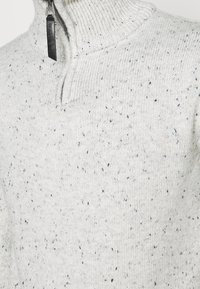 Maglione grigio chiaro lavorato a maglia con il collo a mezza zip, caratterizzato da una texture scarificata e un colletto a coste. Tessuto resistente con un design informale.