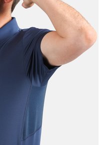 Mörkblå pikétröja med korta ärmar, som har en slät yta och en lätt lyster. Sidopanelen visar ett subtilt, texturerat mönster.