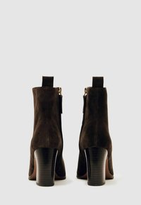 Melnas zamšādas potītes zābaki ar augstu blokveida papēdi, ar rāvējslēdzēju un aizmugurējo cilpu, kas atvieglo uzvilkšanu. Gluda tekstūra, vienkārša dizaina.