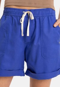 Blå bomullsshorts med dragsko i midjan, sidofickor och uppvikta fållar. Slät textur med en avslappnad design.
