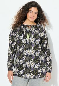 Tunic a maniche lunghe nera con motivi geometrici e floreali multicolori; presenta un collo a legare e frange verdi. Texture del tessuto morbida.