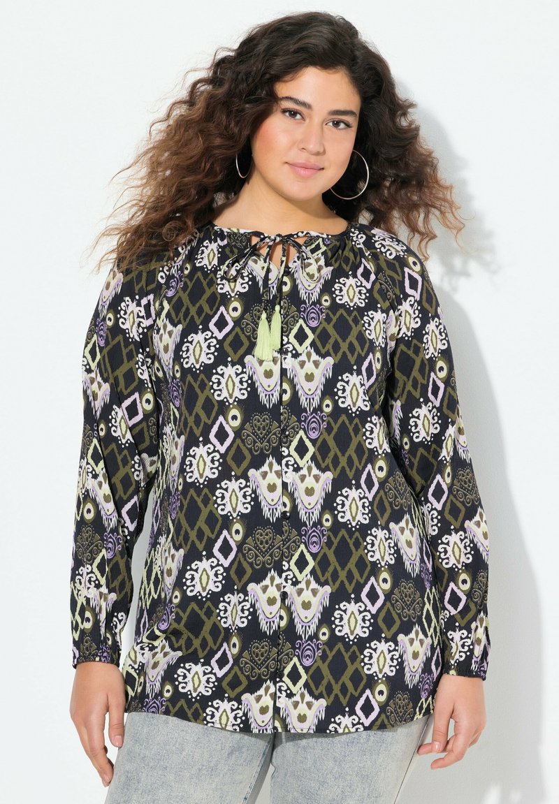 Tunic a maniche lunghe nera con motivi geometrici e floreali multicolori; presenta un collo a legare e frange verdi. Texture del tessuto morbida.