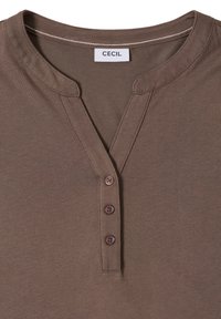 Chemise marron avec encolure ronde, trois boutons marron sur la patte de boutonnage, et étiquette de marque "CECIL" cousue à l'intérieur du col.