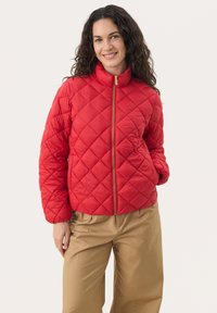 Red quilted puffer jacket with a high collar and gold zipper, featuring a diamond pattern and elastic cuffs. Paired with beige pants.
