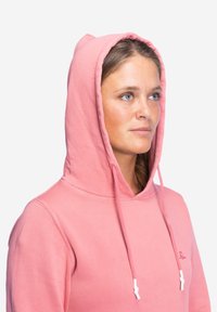 Rosa Kapuzenpullover mit Kordelzug, aus weichem Baumwollmaterial und mit gerippten Bündchen. Mit einem kleinen Logo auf der Brust.