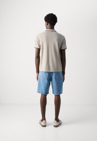 Cămașă polo gri cu detalii în jurul gulerului de culoare bleumarin, asociată cu pantaloni scurți din denim albastru. Textură simplă și croială standard. Încălțăminte casual cu logo.