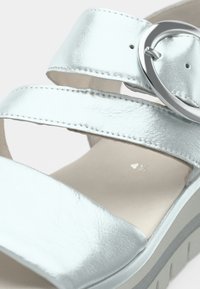 Κοντινό πλάνο ενός λευκού δερμάτινου σανδάλιου με δύο λουριά και ασημένια οβάλ αγκράφα σε ανοιχτή σόλα.