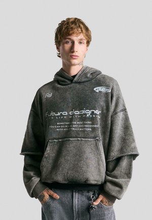 Oversized, gray hoodie with a faded texture and frayed hem. Features text print and two logos on the front, with a kangaroo pocket.