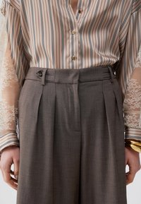 Blouse rayée avec col en V, manches en dentelle transparente. Pantalon plissé taille haute en tissu marron texturé avec détails à boutons.