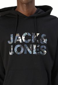 Felpa nera con cappuccio e grande scritta decorata "JACK & JONES" sul davanti. Presenta un cappuccio con cordino e una tasca a marsupio. Materiale morbido.
