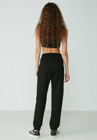 Schwarze, lässig geschnittene Sweatpants mit elastischem Bund und Bündchen. Hergestellt aus weichem Stoff und kombiniert mit einem schwarzen Cropped-Top, das ein schlichtes Design zeigt.