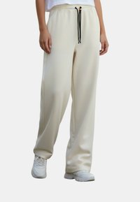 Lichtbeige joggerbroek gemaakt van een glad, rekbaar materiaal. Voorzien van een elastische tailleband met een zwart trekkoord en zijzakken.