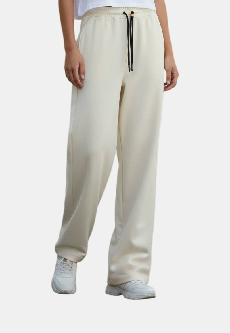 Lichtbeige joggerbroek gemaakt van een glad, rekbaar materiaal. Voorzien van een elastische tailleband met een zwart trekkoord en zijzakken.
