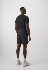 Camiseta negra y pantalones cortos de tela ligera. La camiseta tiene mangas cortas; los pantalones cortos cuentan con una cinturilla elástica y bolsillos laterales.