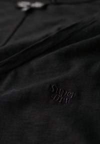 Black cotton t-shirt with a soft texture, featuring an embossed "Super DIY" logo on the bottom left side. Simple and minimal design.