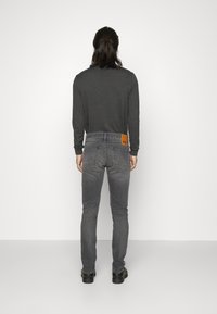 Jeans de mezclilla gris con ajuste slim, que cuentan con un parche de cuero marrón en la parte posterior de la pretina y una tela lisa y con textura.
