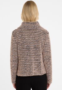 Strickjacke aus beigem und schwarzem Garn mit einem strukturierten, gestreiften Design, das einen hohen Kragen und eine lockere Passform aufweist.