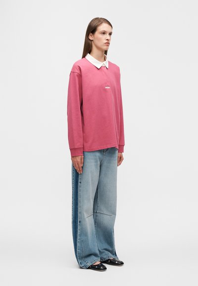 Ροζ πουκάμισο πόλο με μακριά μανίκια και λευκό γιακά· φαρδιά ανοιχτόμπλε τζιν παντελόνια. Απλός σχεδιασμός με ελάχιστες λεπτομέρειες και χαλαρή σιλουέτα.