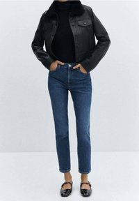 Veste courte en cuir noir avec un col en fourrure, associée à un jean taille haute bleu et des ballerines noires. Design simple, sans motifs.