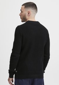 Suéter negro de punto con un patrón texturizado, de manga larga, con puños y dobladillo acanalados. Presenta un escote redondo y una pequeña etiqueta de marca en el lateral.
