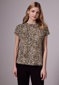 Top de manga corta con estampado de leopardo en beige y manchas negras. Escote redondo y corte relajado, fabricado en tejido suave, combinado con pantalones oscuros.