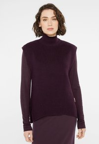 Violetter Rollkragenpullover mit geripptem Muster und Schulterdetails, kombiniert mit einer glatten, langärmligen Unterlage in einem passenden Farbton.