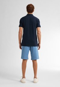 Navy polo tričko s krátkými rukávy, kombinované se světle modrými šortkami vyrobenými z měkké látky, obuté s krémovými teniskami.