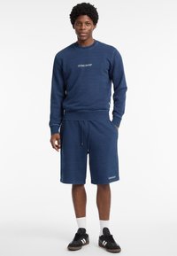 Marineblauwe set van een sweat shirt en shorts, gemaakt van zachte stof, met een ronde halslijn, ribgebreide manchetten en een logo op de borst en onderkant.