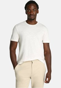 T-shirt in cotone bianco con maniche corte, scollatura rotonda, vestibilità rilassata, texture liscia, abbinato a pantaloni beige.